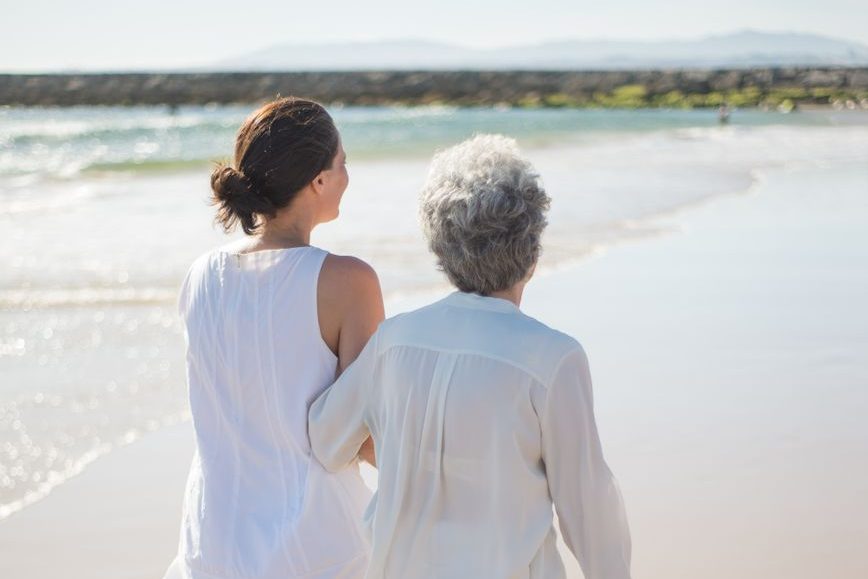 elderly woman holding on another woman while walking at the beach
