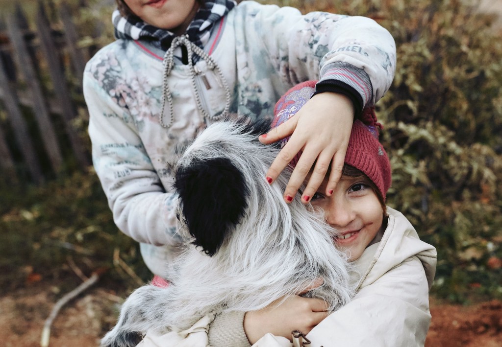 Two young kids hugging a dog.